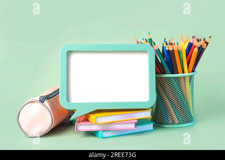 Federmäppchen, Notizbücher, Buntstifte im Glas und Rahmen mit Platz für Text auf grünem Hintergrund. Wieder-in-die-Schule-Konzept Stockfoto