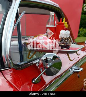 Ein 1950er Chevrolet Cabrio, das auf einer Autoshow ausgestellt wird, bietet ein Autokino-Restaurant mit Fensterteller und Fast Food und Getränken. Stockfoto