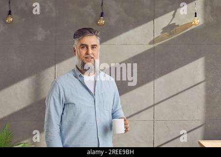 Ein hübscher, grauhaariger Mann mit Bart und weißer Tasse Stockfoto