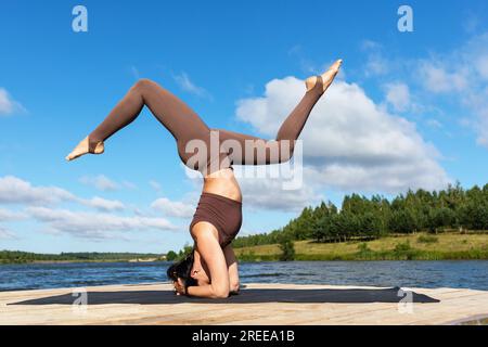 Eine Frau, die Yoga praktiziert, eine Variation des Shirshasana-Trainings, umgekehrtes Asana, Kopfstand und Handstand, trainiert Sportbekleidung an der Küste Stockfoto