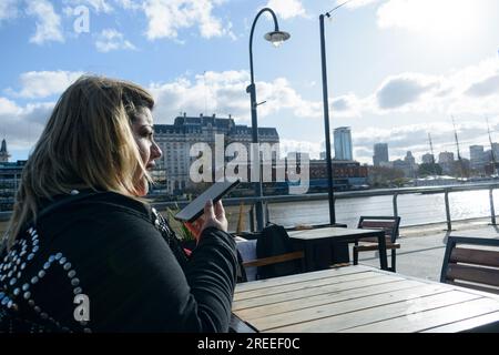 Junge, übergroße latina, die vor dem Restaurant sitzt, eine Sprachnotiz mit ihrem Telefon schickt, mit ihren Freunden kommuniziert, ein technisches Konzept Stockfoto