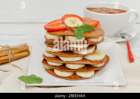 Stapel Keto-Pfannkuchen mit Banane und Erdbeeren auf dem unteren Becher mit Schokolade Stockfoto
