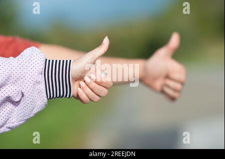 Detailansicht zweier Anhalter, weiblich und männlich, mit hochgezogenen Fingern, per Anhalter an einem sonnigen Tag. Autostop-Konzept Stockfoto