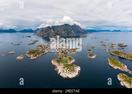 Luftaufnahme, Henningsvaer mit Fußballfeld, felsige Inseln im Meer vor Bergen, Festvagtinden, Vestvagoy, Lofoten, Norwegen Stockfoto