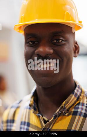 Ein afroamerikanischer Lagerarbeiter trägt einen Schutzhelm im Porträt. Lächelnder Lagerladen mit fröhlichem Gesichtsausdruck in industrieller Schutzausrüstung mit Blick auf Kameranah Stockfoto