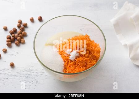 Glasschale mit Grieß, Eiern, geriebenen Karotten, Zucker, Salz und Backpulver. Kochen von Mannik, Kuchen oder Kuchen auf hellblauem Hintergrund. Schritt für Schritt, C. Stockfoto