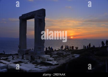 Insel Naxos, Touristen bewundern den Eingang des Apollo-Tempels bei Sonnenuntergang. Marmortür, die allein am Meer steht, bei Sonnenuntergang. Stockfoto