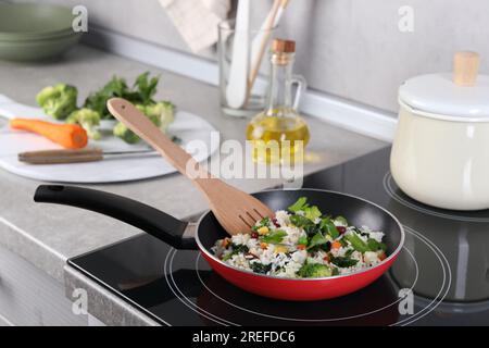 Schmackhaften Reis mit Gemüse auf dem Induktionsherd in der Küche braten Stockfoto