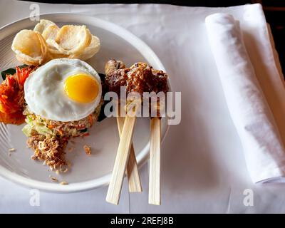 Gebratener indonesischer Reis Nasi Goreng serviert mit Sojasoße, Chilipasta, Sambal, sonniger Seite nach oben, Satay, Sate, Hühnerspieß und Kerupuk-Cracker Stockfoto