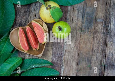 Frische Guaven mit grünen Blättern auf Holzhintergrund. Konsistenz von Holz und Guavablättern. Stockfoto