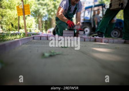 Einer der Deckenfertiger legt Pflastersteine und der andere bringt ein paar Stücke mit. Stockfoto