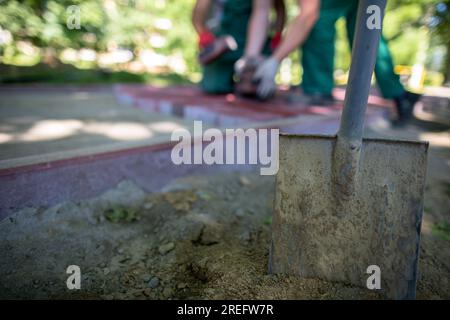 Im Vordergrund, eine Schaufel im Boden und Bauarbeiter im Hintergrund. Stockfoto
