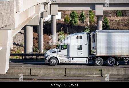 Industrielles weißes großes Rig mit hoher Fahrerkabine für Lkw-Fahrer, Rest-Sattelzugmaschine für den Transport von gewerblicher Fracht in einem Kühlanhänger, der auf der Autobahn fährt Stockfoto