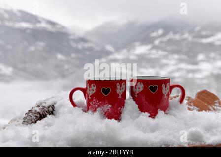 Zwei rote Tassen mit Herzform im Schnee- und Berghintergrund Stockfoto
