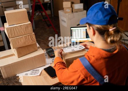 Logistikzentrum oder Lagerhauskonzept für den Lagerbetrieb, Lagerarbeiter. Junge Frau, die Produkte während der Arbeit im etikettiert Stockfoto