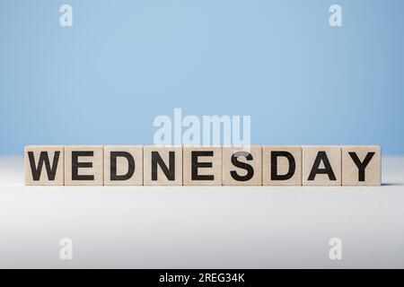 Text Wednasday auf Holzwürfeln auf blauem Hintergrund. Wochentag auf Holzblöcken. Webbanner für Wochentage. Ursprünglicher Kalender. Teil der Serie. Zeitkonzept Stockfoto