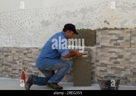 Bild eines Handwerkers, der mit einem Pfannenwender den Klebstoff ausstreut, um die Fliesen an einer Hauswand zu verlegen. Heimarbeit und Hausrenovierung. Stockfoto