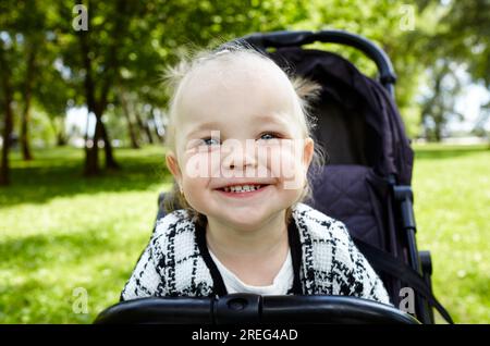 Baby im Kinderwagen auf einem Spaziergang im Sommerpark. Ein bezauberndes kleines Mädchen, das im Kinderwagen sitzt und lächelt. Kind im Buggy Stockfoto