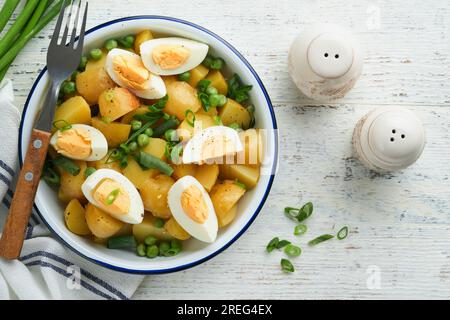 Traditioneller Kartoffelsalat mit Speck und Eiern in einer weißen Schüssel. Picknick-Food-Konzept. Schüssel mit warmem Kartoffelsalat. Deutscher Kartoffelsalat. Draufsicht. Stockfoto