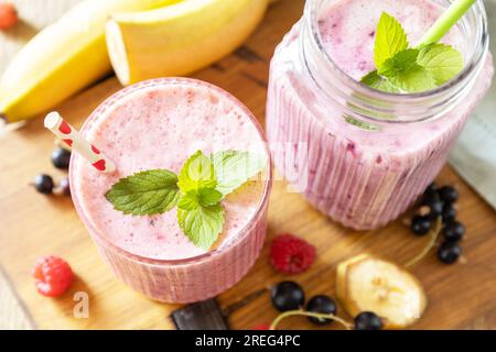 Set aus frischen, verschiedenen köstlichen Milchshakes oder Smoothies mit frischen Beeren auf rustikalem Hintergrund. Himbeeren und schwarze Johannisbeere. Stockfoto