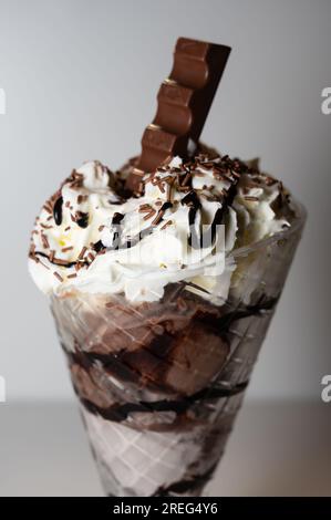 Schokoladeneis in einem großen Eisbecher mit 3 Kugeln Eiscreme sowie verschiedenen Saucen und Belägen. Stockfoto