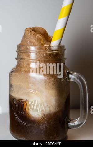 Vanille-Eiscreme-Float, serviert in einem Milchglasbecher mit gelbem gestreiftem Strohhalm. Stockfoto