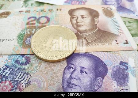 Nahaufnahme einer goldenen Bitcoin-Münze auf einem Stapel chinesischer Yuan-Banknoten. Stockfoto