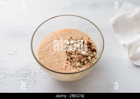 Glasschüssel mit Teig für Karotten-Grieß-Kuchen, Mannik mit Nüssen. Kochen auf hellblauem Hintergrund. Schritt für Schritt, Kochschritt Stockfoto