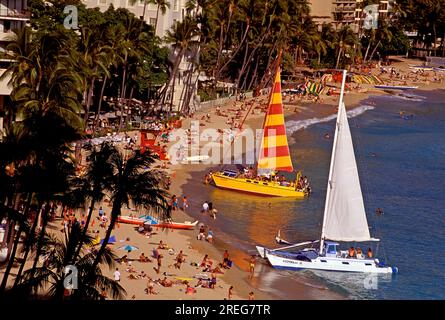 Die Touristenmassen entspannen sich am wunderschönen Waikiki Beach mit zwei großen Katamaranen an der Küste. Stockfoto