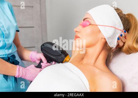 Porträt einer schönen Frau in Schutzbrille beim Laser-Haarentfernungsverfahren im Schönheitssalon. Kosmetikerin epiliert Achselhöhlen. Konzept Stockfoto