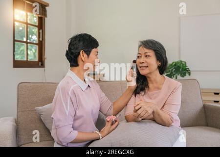 Glückliche Seniorenfreunde, die im Wohnzimmer Make-up-Spaß machen, Selbstpflegekonzept Stockfoto
