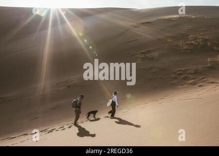 Zwei Wanderer und ihr Hund folgen den Fußspuren in den Sanddünen Stockfoto