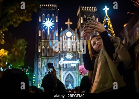Eine junge vietnamesische Frau macht am späten Heiligabend ein Selfie vor der dekorierten katholischen St. Jospeh's Cathedral im Herzen von Hanoi, Vietnam. Stockfoto