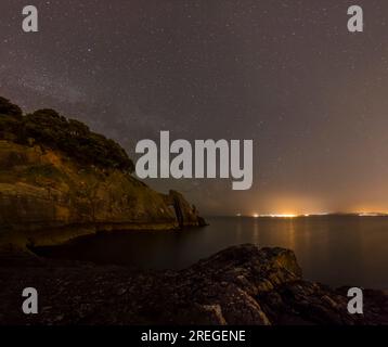 Natürlicher Meeresbogen und Küste bei Nacht mit Sternenhimmel und Lichtern Stockfoto