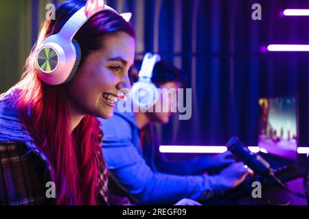 Eine Frau lächelt glücklich, während sie mit einem männlichen Spieler an Videospielen teilnimmt. Gamerinnen tragen ein Headset und sitzen vor einem Mikrofon, Live-Aufnahme Stockfoto