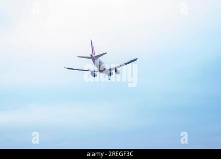 Low-Angle-Sicht auf kommerzielle Flugzeuge, die im Himmel fliegen, mit Fahrwerk, das am Flughafen startbereit ist Stockfoto
