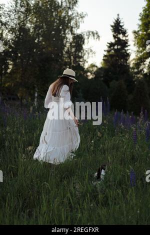 Junge Frau in einem Kleid und Hut in einem lupinen Feld, rustikaler Stil. Stockfoto