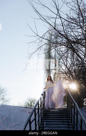 Das Mädchen geht bei Sonnenuntergang in einem langen Kleid die Treppe hinunter Stockfoto