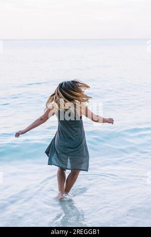 Eine junge Frau dreht sich bei Sonnenaufgang am ruhigen Strand. Stockfoto