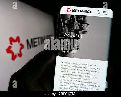 Person, die ein Mobiltelefon hält, mit Website des Stahlunternehmens Ukrainian Metinvest Holding LLC auf dem Bildschirm mit Logo. Konzentrieren Sie sich auf die Mitte des Telefondisplays. Stockfoto