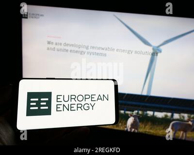 Person, die ein Mobiltelefon mit dem Logo des dänischen Unternehmens European Energy für erneuerbare Energien AUF dem Bildschirm vor der Webseite hält. Konzentrieren Sie sich auf das Display des Telefons. Stockfoto