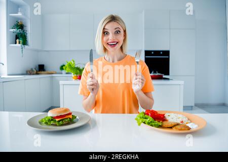 Foto von erstaunlich charmanten Mädchen Hände halten Messer Gabel Reis Fleisch Gemüse Burger Teller Küche Tisch Wohnung drinnen Stockfoto