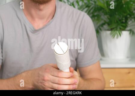 Der Typ entfernt Haare und Wolle vom T-Shirt mit einem Fusselroller. Ein Mann mit einer Haarentfernungswalze. Stockfoto