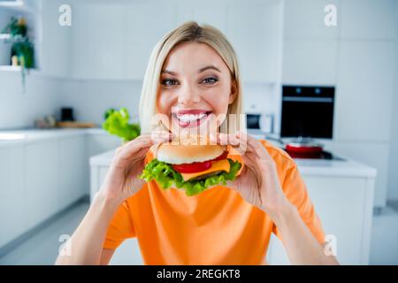 Porträt von süßer, fröhlicher Lady, mit einem Lächeln Hände halten, genießen Sie einen großen hausgemachten Burger, helles Küchenhaus drinnen Stockfoto