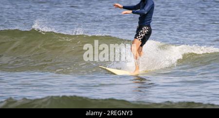 Ein männlicher Surfer reitet auf einer kleinen Welle auf seinem Surfbrett aus der Nähe. Stockfoto