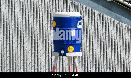 Eine blaue Wasserkanne auf einem dreibeinigen Ständer an der Seite der Tribüne, damit Sportler Wasser bekommen können. Stockfoto