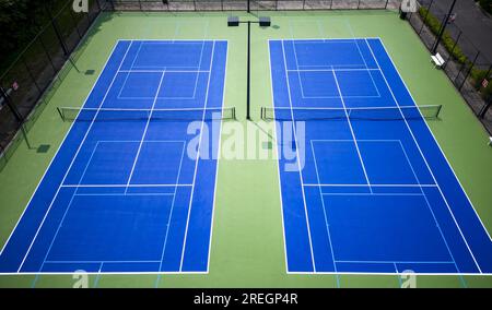 Zwei blaue und grüne Pickleball und Tennisplätze, von einer Drohne aus gesehen, mit Lichtern und einem schwarzen Zaun rund um die Plätze Stockfoto