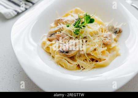 Pasta Alfredo Fettuccine mit Huhn, Champignon-Pilzen, Parmesan auf hellem Hintergrund. Stockfoto