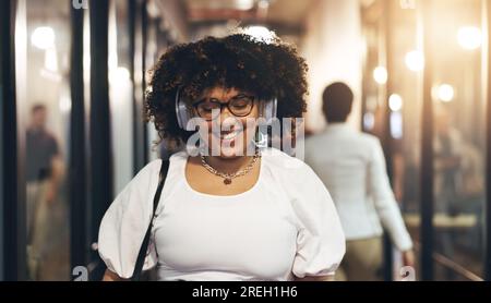 Kopfhörer, glücklich und das Gesicht einer Frau im Büro, die mit ihren Kollegen zum Schreibtisch geht. Begrüßung, Lächeln und Porträt einer weiblichen Kreativin Stockfoto