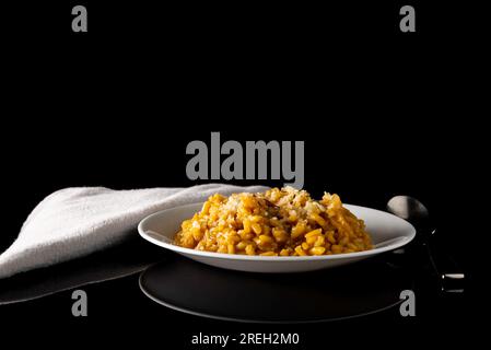 Weiße Platte mit gelbem Risotto-Reis auf schwarzem Hintergrund mit Löffel und Serviette Stockfoto